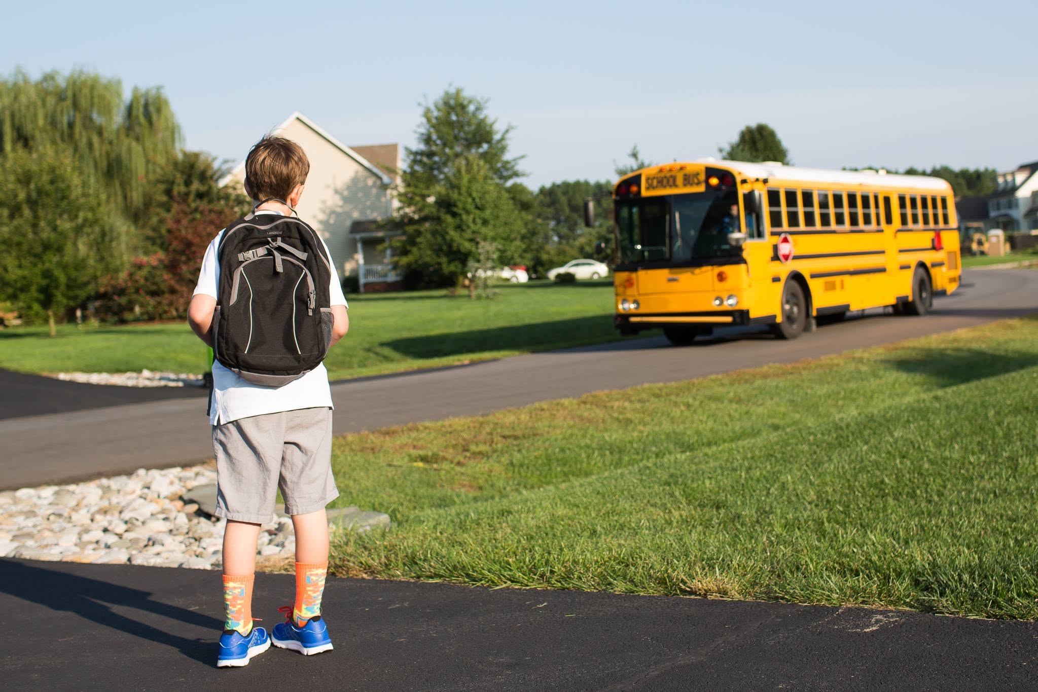 A student with a backpack waiting for a yellow school bus in a neighborhood